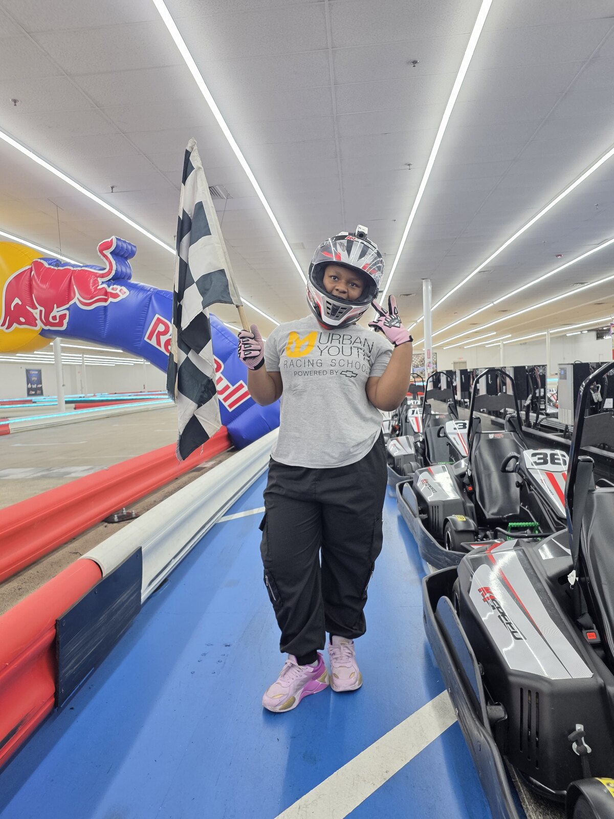 Young UYRS student in racing gear holding a checkered flag at the kart track
